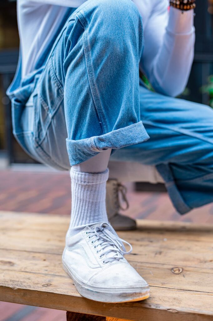 Close-up of a casual outfit featuring denim overalls and white sneakers.