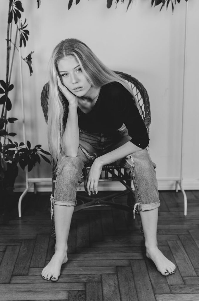Black and white portrait of a woman sitting barefoot indoors, exuding contemplation.