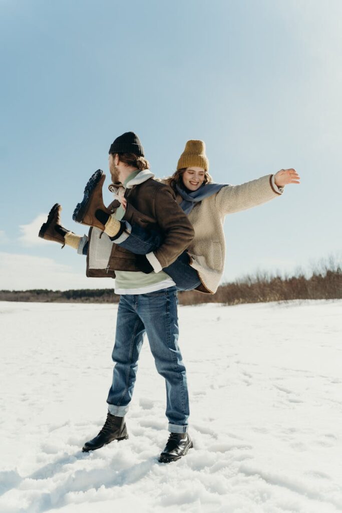 Happy couple having fun in winter snow wearing cozy clothes. Joyful outdoor moment.