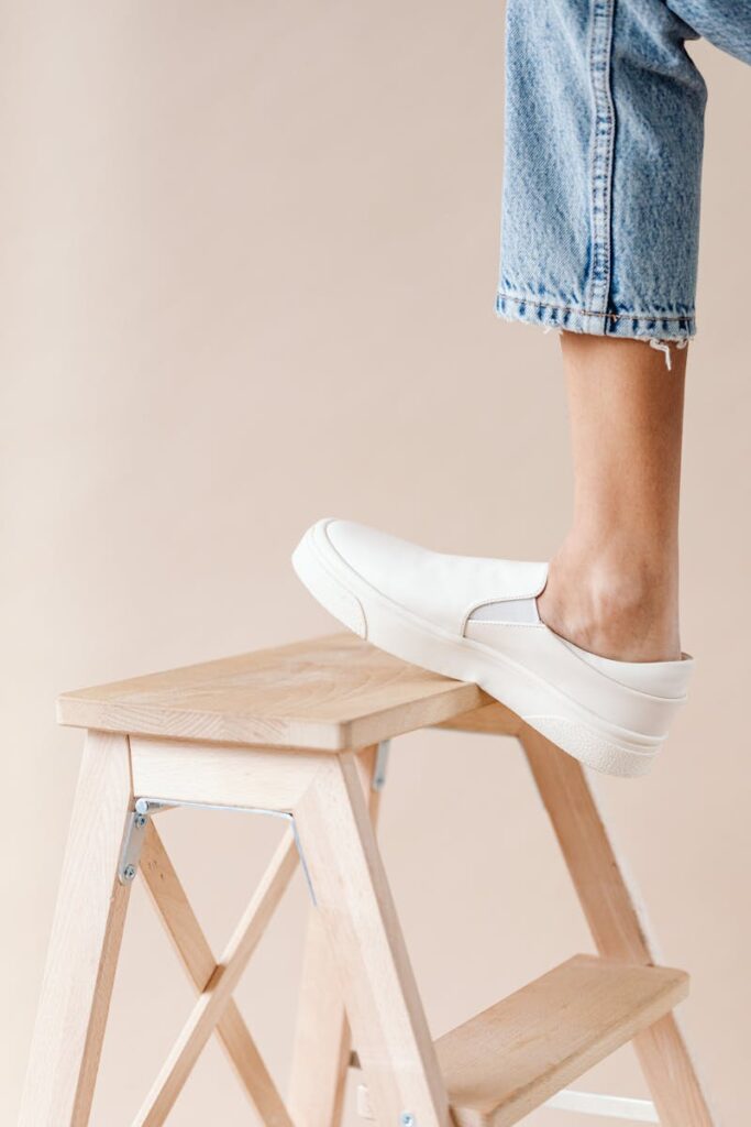 Stylish white sneakers on a wooden ladder with a minimalist beige background.