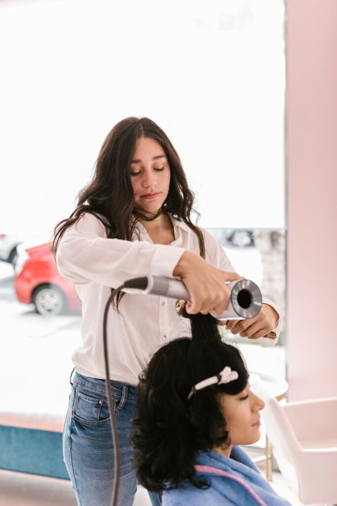 A hairstylist uses a blow dryer on a client's hair in a contemporary salon setting.