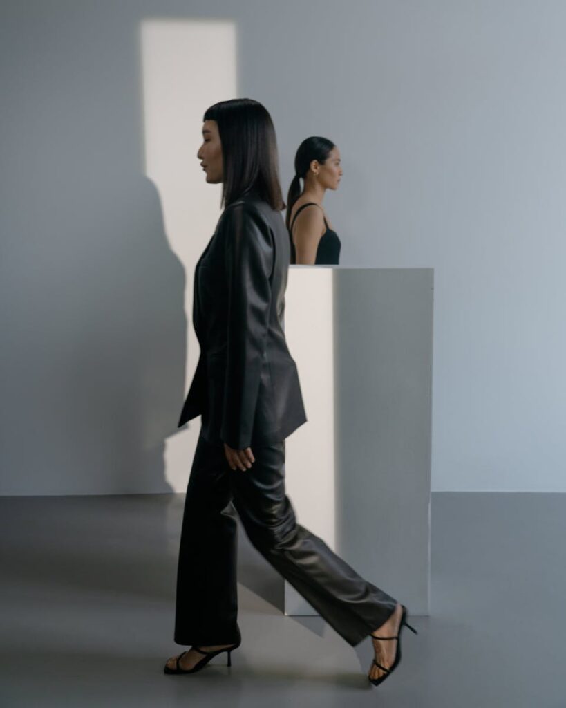 Stylish women in black attire walking and posing in a minimalistic studio with soft lighting.