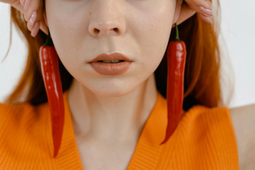 Close-up of a woman's face wearing unique chili pepper earrings in a vibrant orange attire.