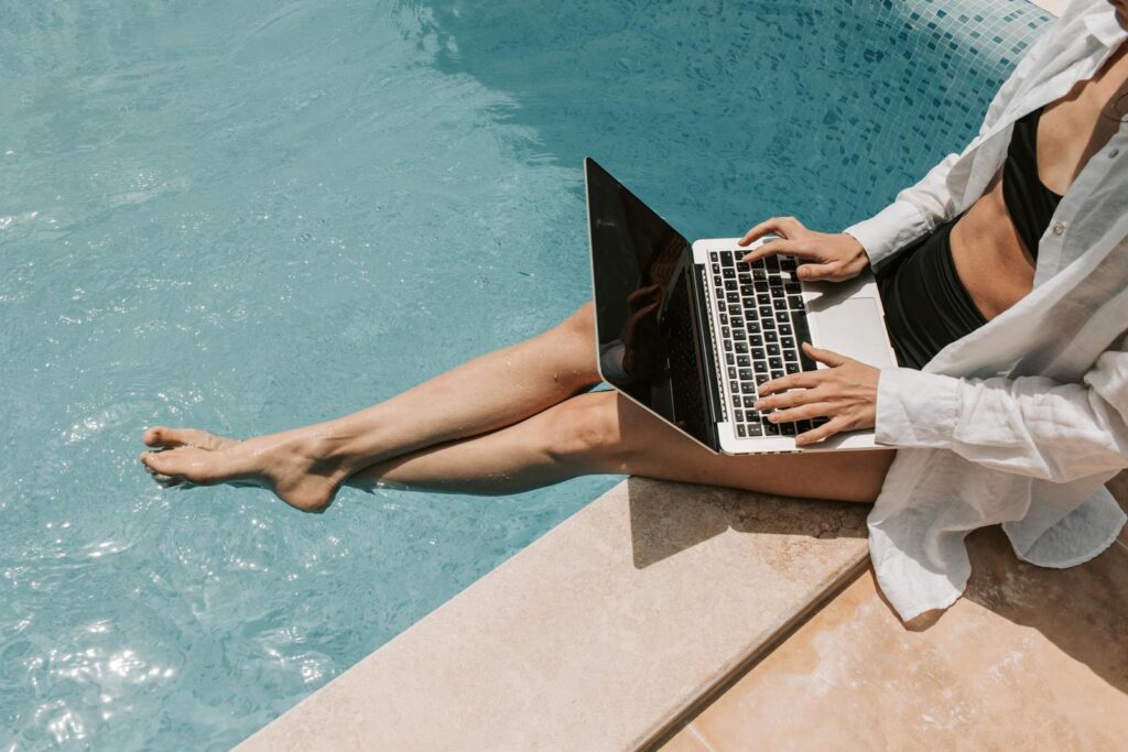 A woman in swimwear working on a laptop by the pool, showcasing summer remote work lifestyle.