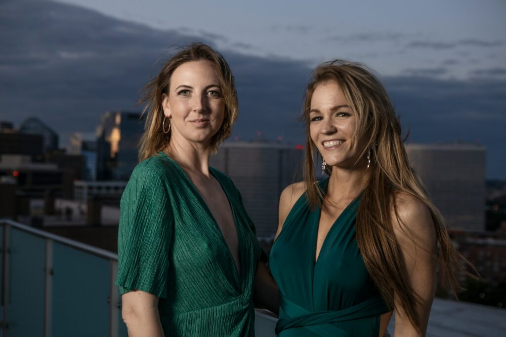 2 women in green v neck shirt standing near body of water during daytime