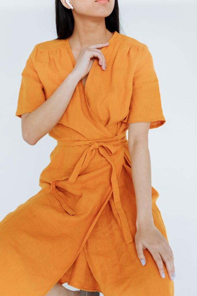 Elegant woman posing in vibrant orange dress with minimal background.