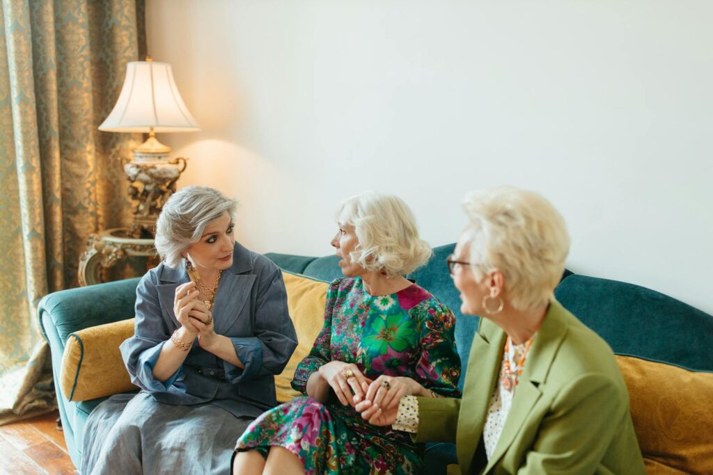 Three elegant senior women having a lively conversation indoors, showcasing friendship and fashion.