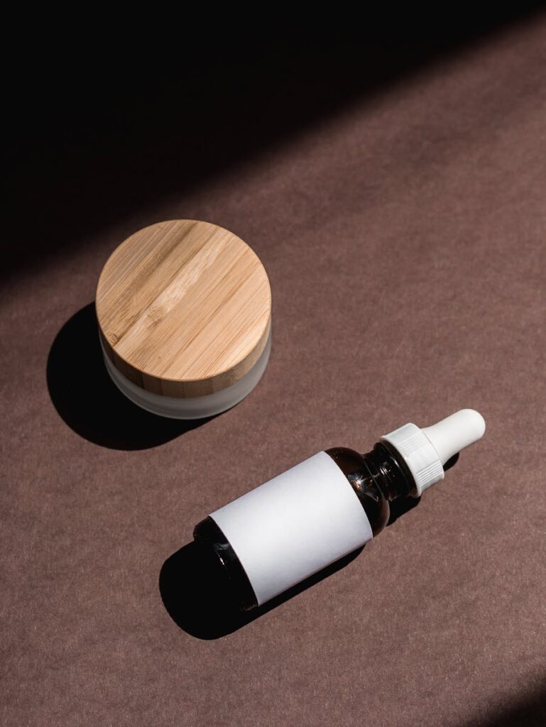 Aesthetic flat lay of a serum bottle and jar on a brown surface with natural lighting.