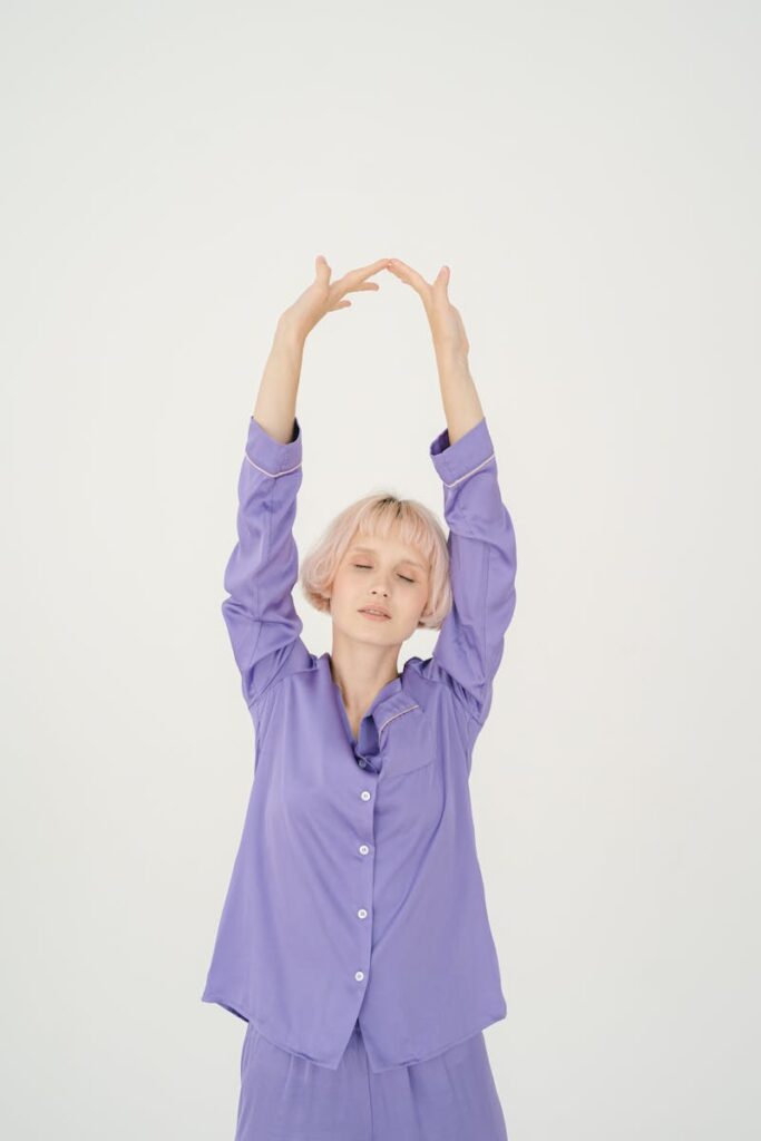 A woman with eyes closed stretching in purple pajamas, conveying morning relaxation.