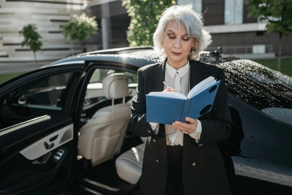 Senior businesswoman writing in notebook next to a car outside a modern building.