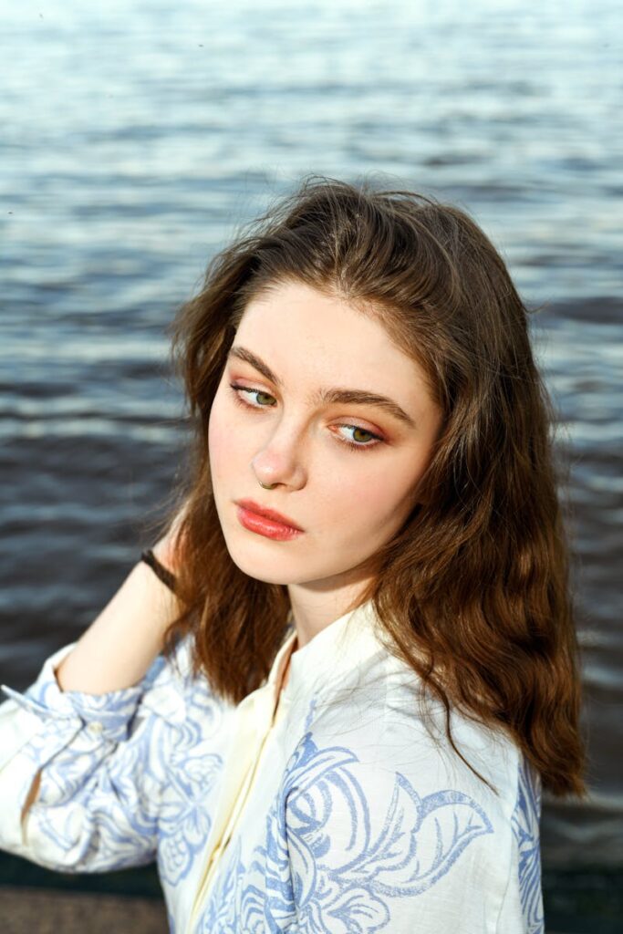 A serene portrait of a woman with long hair looking away by the sea, creating a tranquil and contemplative mood.