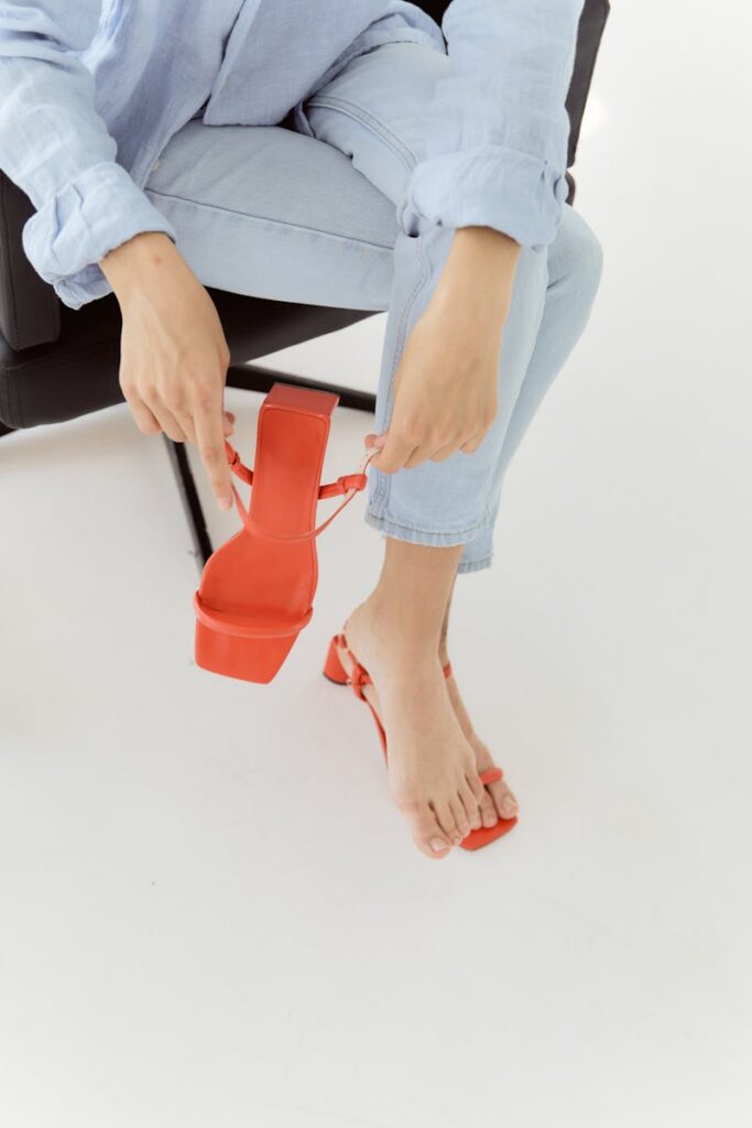 Close-up of a woman adjusting red sandals while wearing denim jeans. Fashionable and chic footwear style.