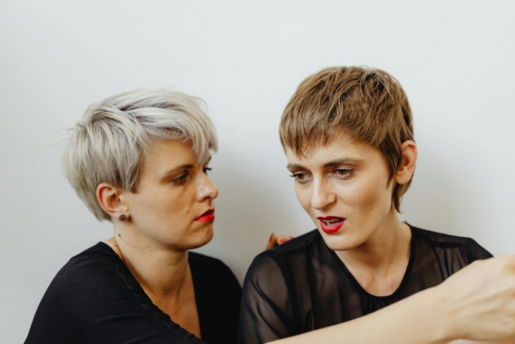 Two women with short hairstyles having an intense discussion indoors against a white wall.