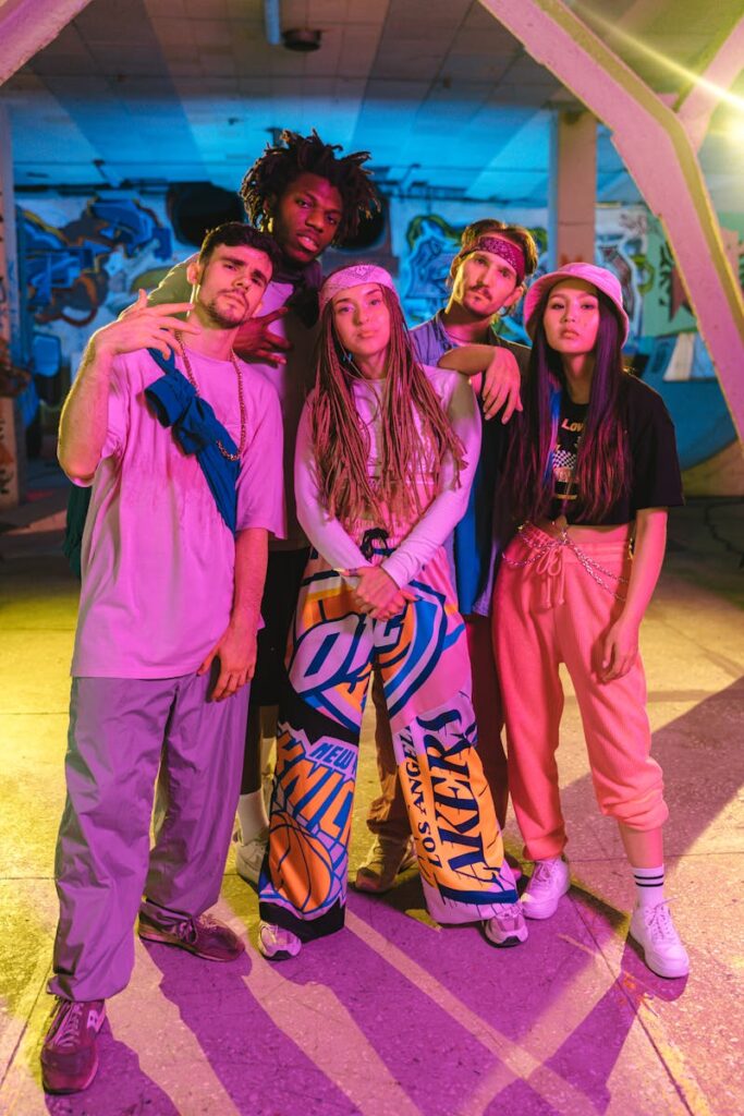 Stylish group of diverse young adults wearing vibrant streetwear in an urban setting under colorful neon lights.