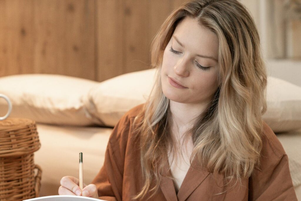 A woman in brown attire writing in a cozy indoor environment with soft lighting.