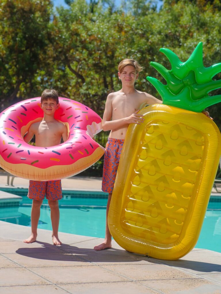 Two boys holding colorful pool floats by a swimming pool on a sunny day.