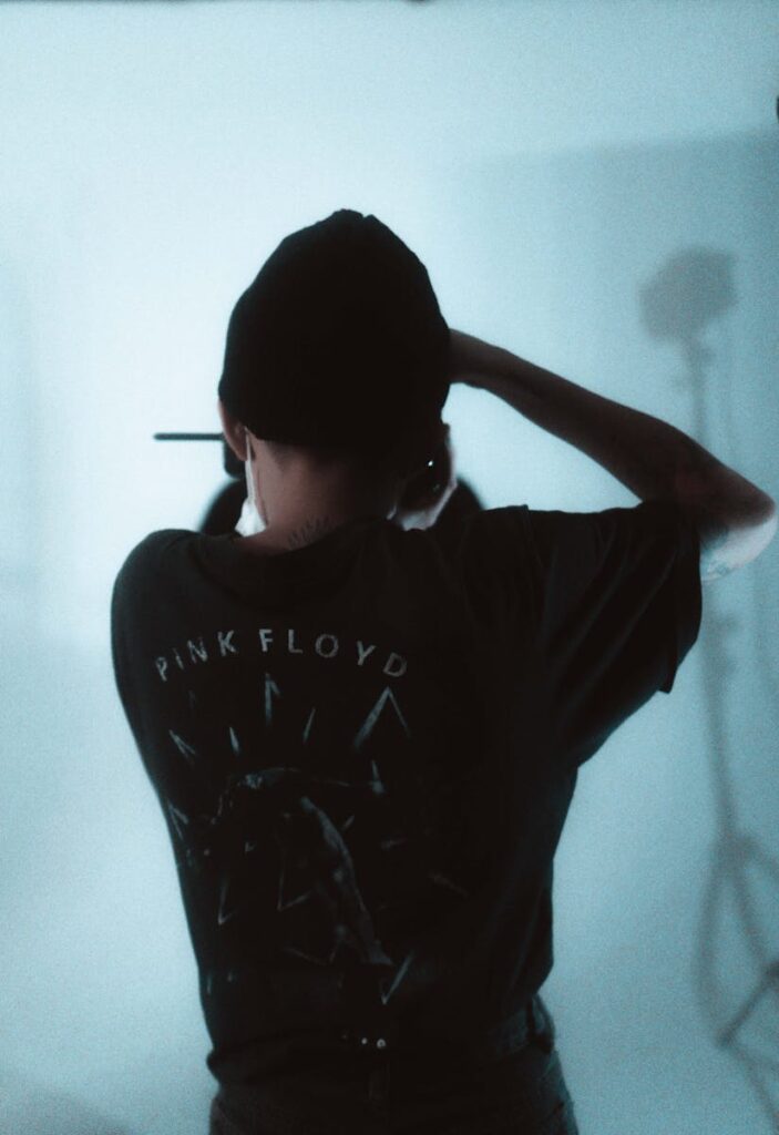 Back view of a person wearing a Pink Floyd shirt, adjusting hair in a studio setting.