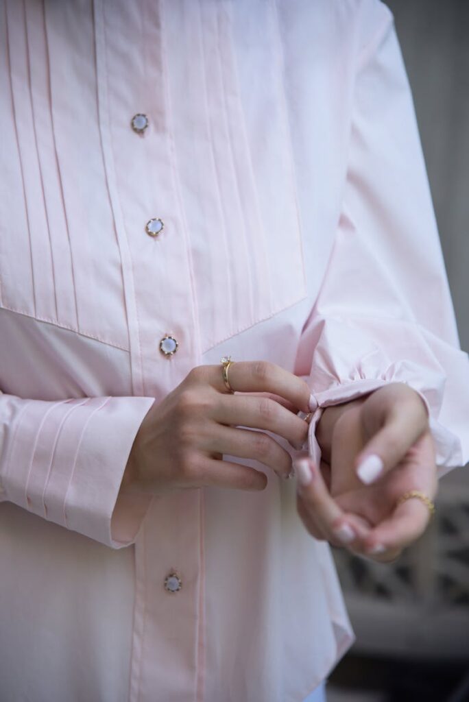 Close-up of a woman adjusting the cuff of a pink shirt with decorative buttons.