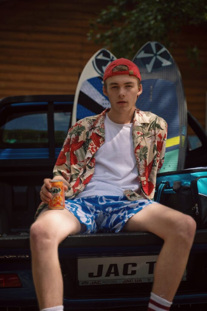 Teenage boy relaxing on a car trunk with a canned drink, enjoying a sunny day.