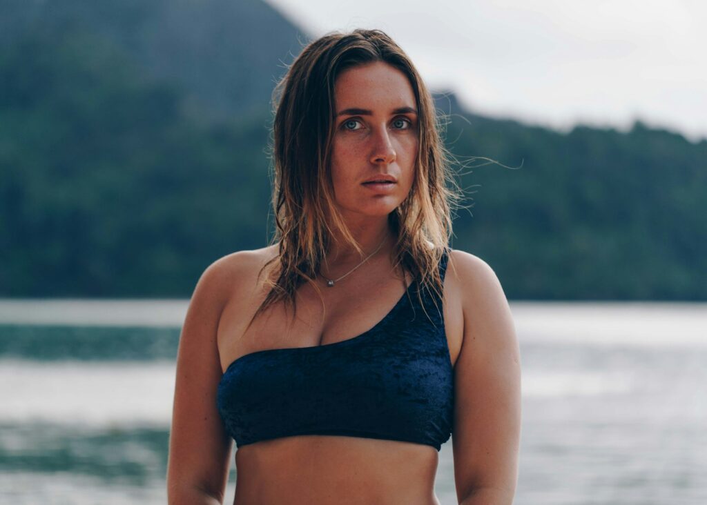 selective focus photography of standing woman wearing gray bra on seashore during daytime
