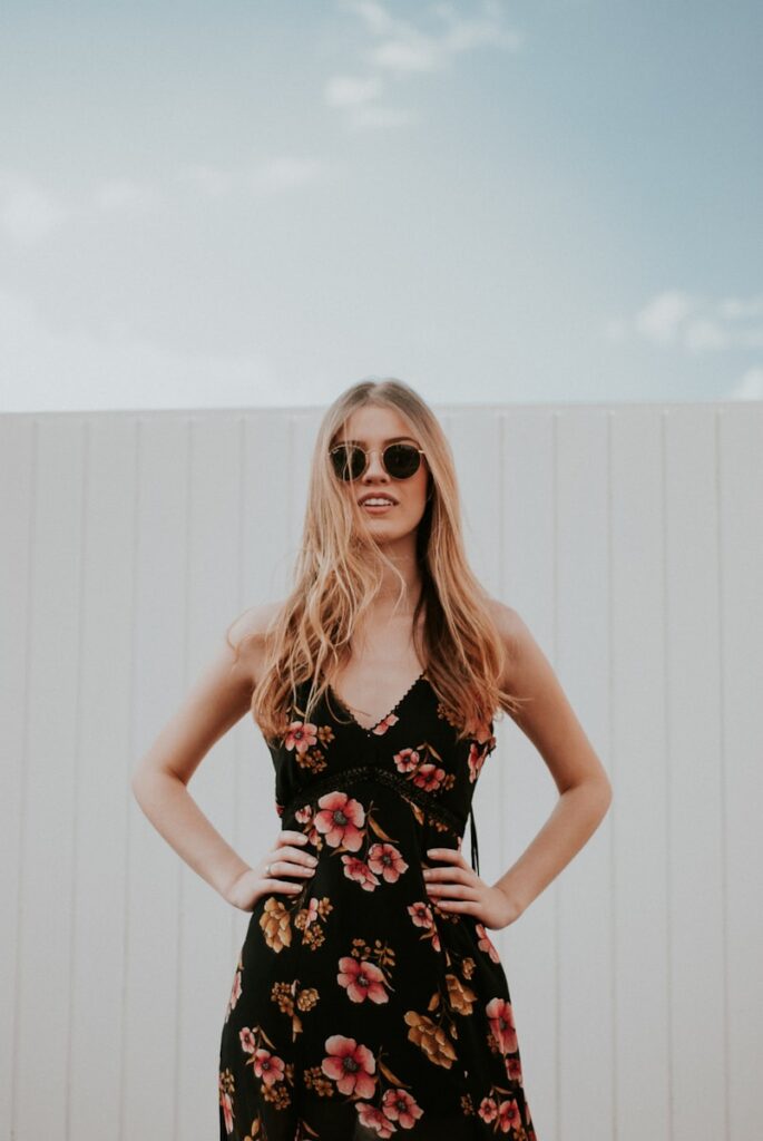 woman wearing black sunglasses standing near white wooden wall