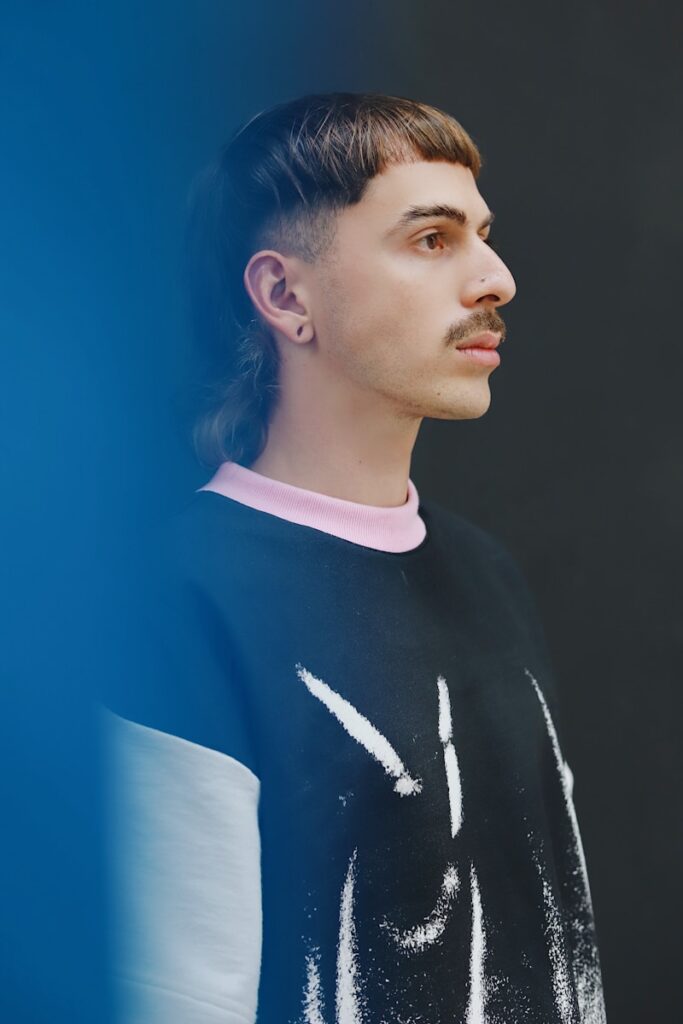a man with a moustache standing in front of a blue wall