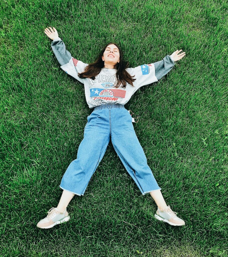 woman in white long sleeve shirt and blue denim jeans lying on green grass field during