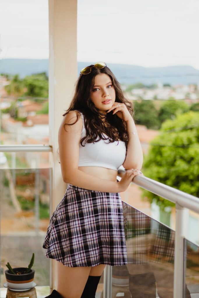 Teenager in crop top and skirt, posing outdoors on a balcony.