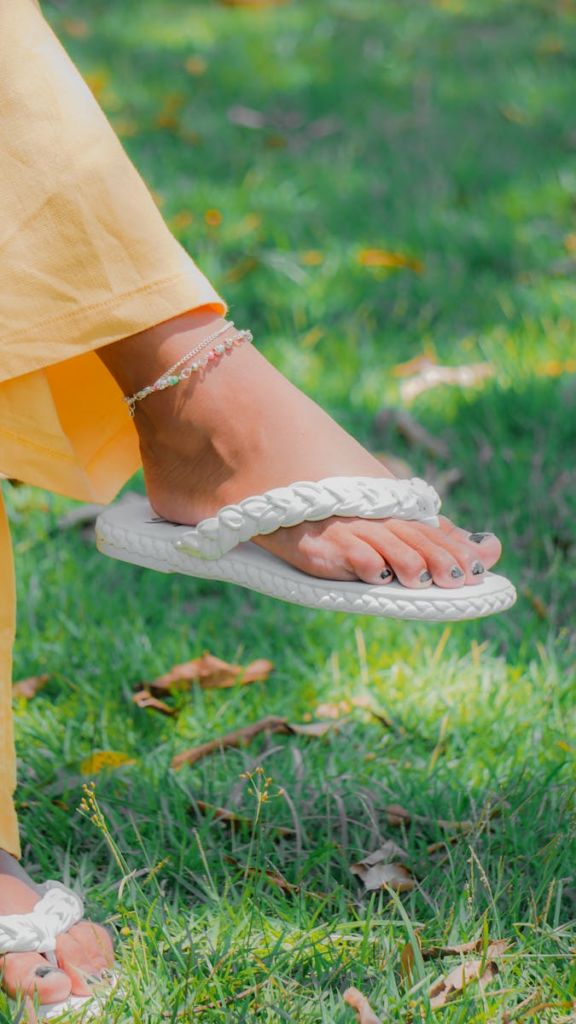 A fashionable foot with an anklet and slippers on green grass, showcasing style and nature.