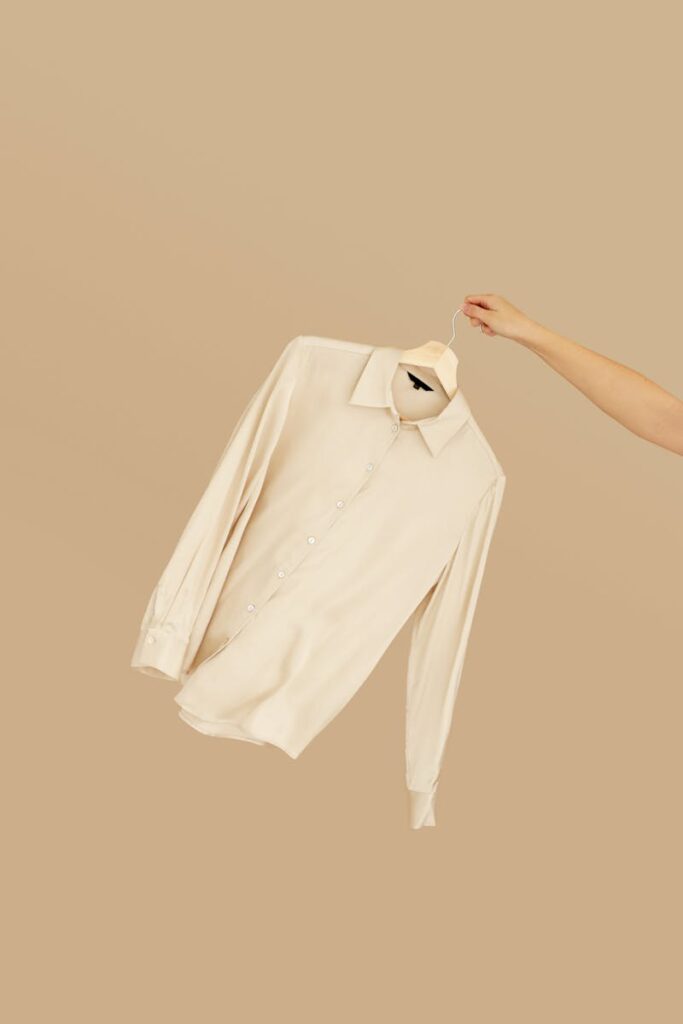 Simple beige dress shirt suspended on a hanger in a minimalist setting.