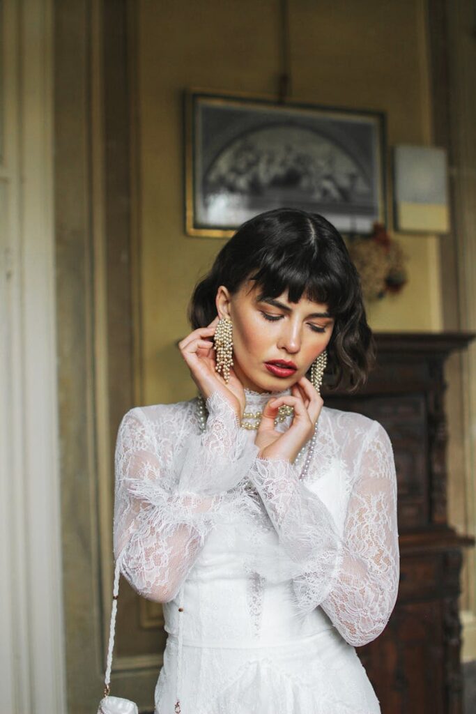 Portrait of a stylish woman in a lace white dress, wearing statement earrings and a pensive expression.