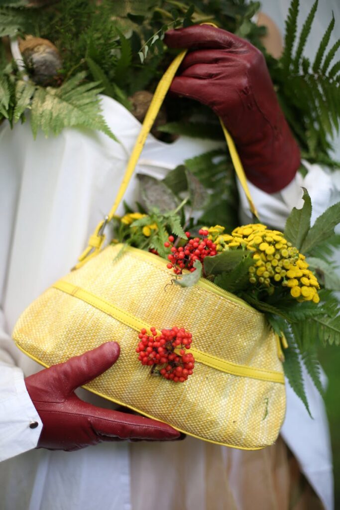 Stylish red gloves holding a yellow handbag filled with autumn flowers and leaves.
