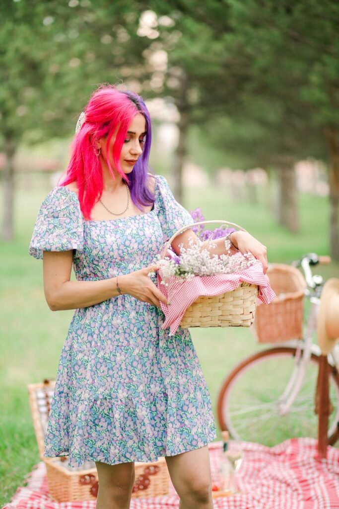 Young woman with colorful hair holding a basket during a picnic in a park.