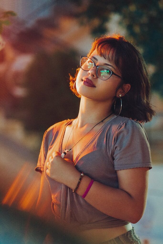 Portrait of a fashionable young woman wearing glasses, embracing a warm sunset glow outdoors.