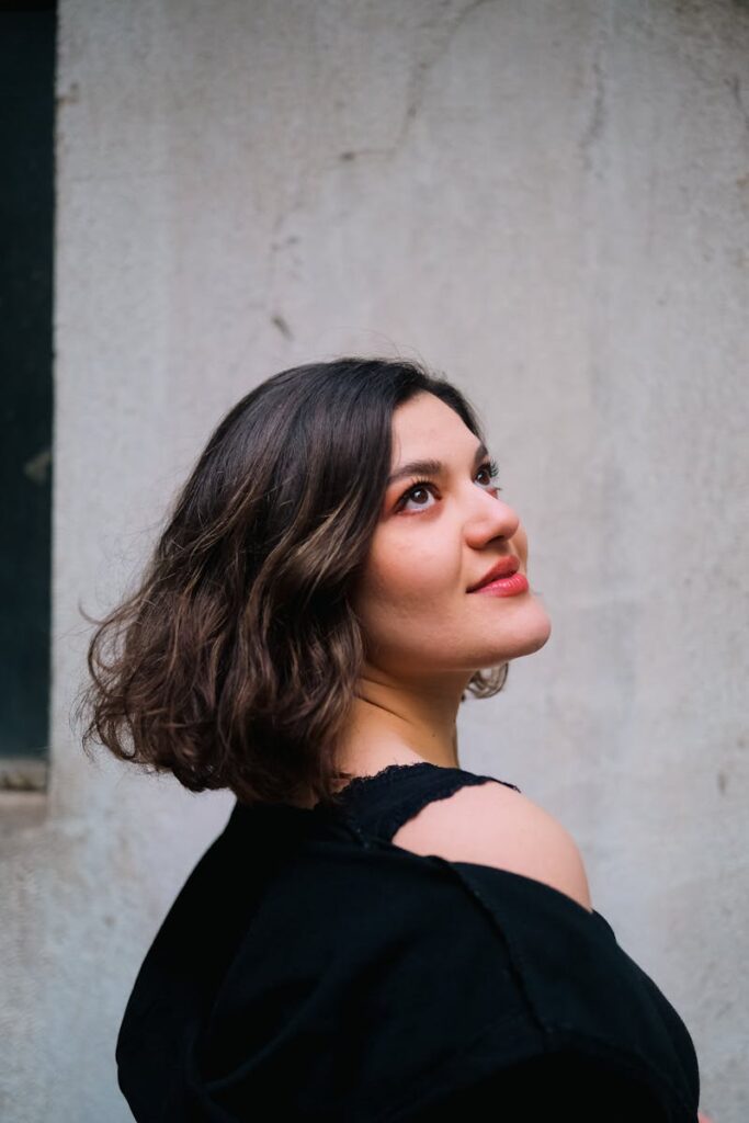 A stylish young woman with short brunette hair gazes upwards in a vertical shot.