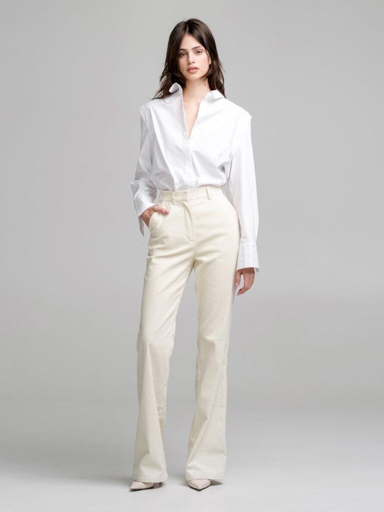 A young woman poses elegantly in a minimalist studio with a stylish outfit.