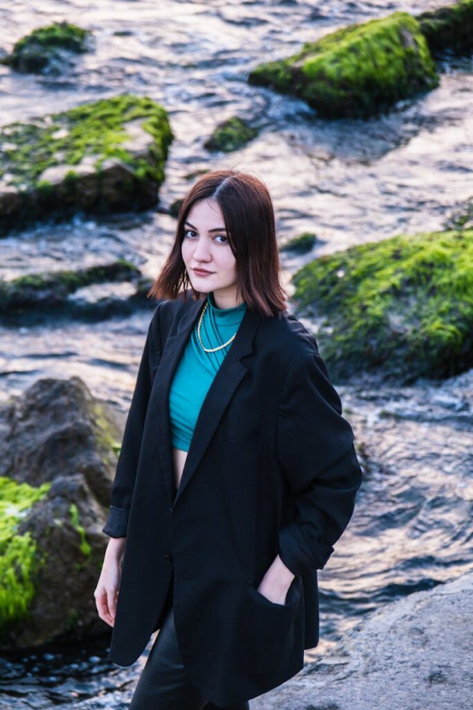 Young woman in a blazer posing by the rocky seashore during sunset.