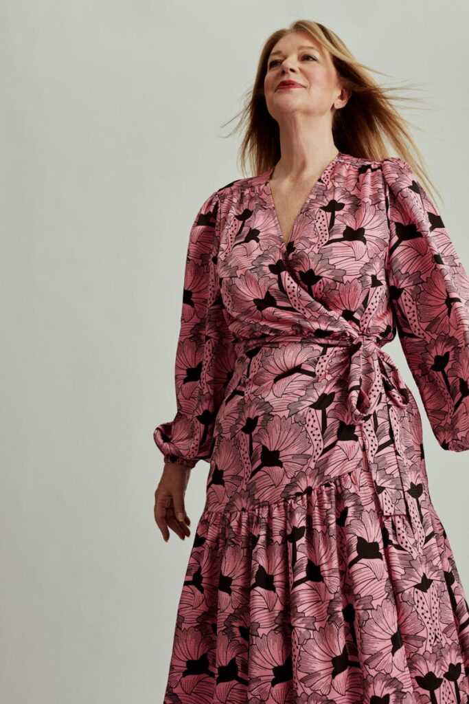 A stylish woman poses in a floral pink dress during a studio photoshoot.