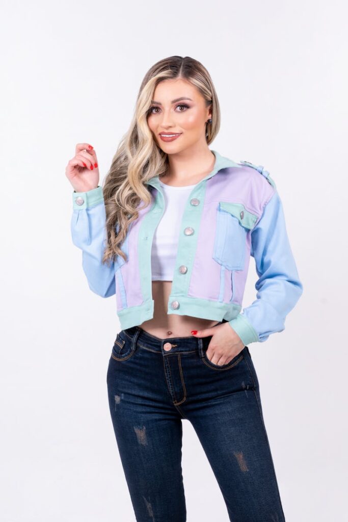 Chic fashion model smiling in pastel jacket and jeans in studio setting.