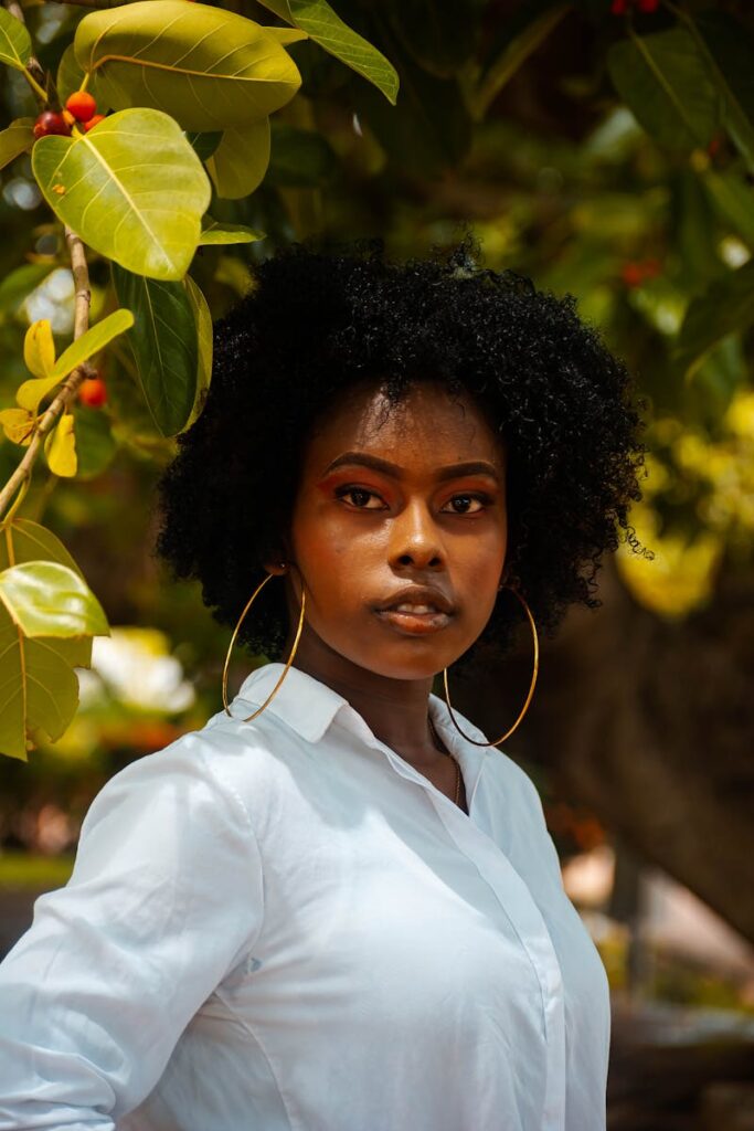Elegant portrait of a woman with natural hair posing outdoors in a white shirt against lush foliage.