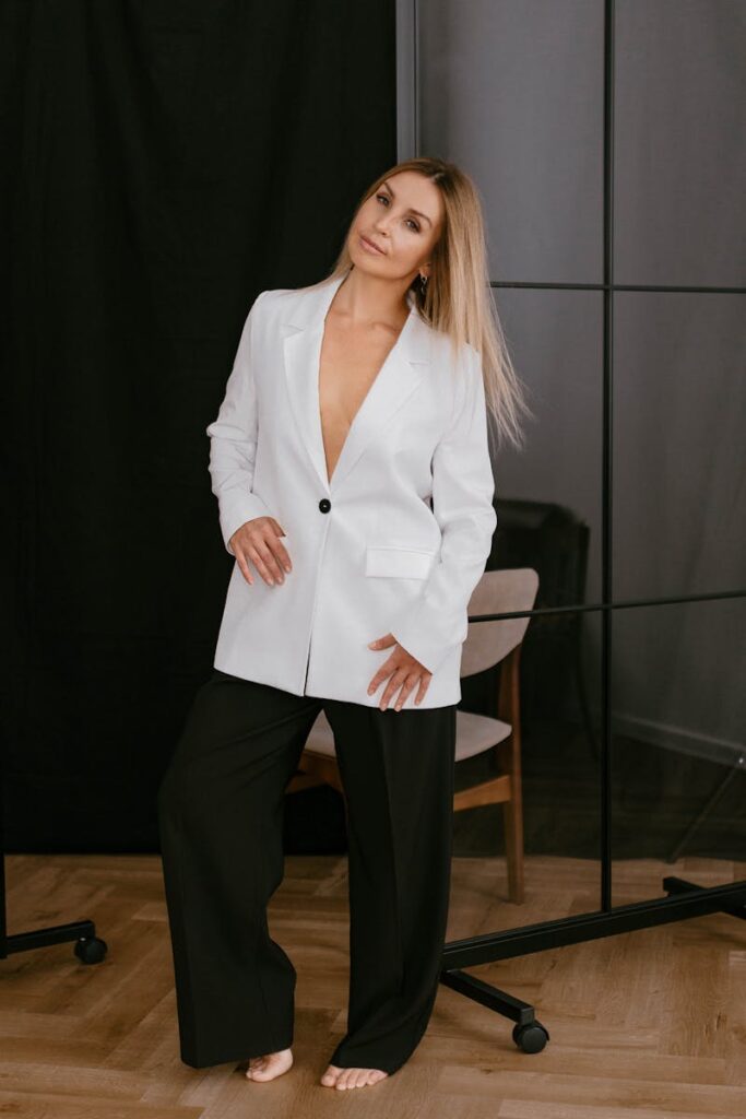 Stylish woman in a white blazer posing gracefully indoors for a fashion shoot.