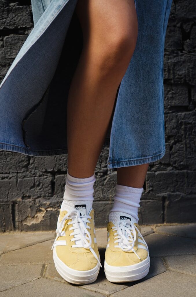 Close-up of a person wearing yellow sneakers and a denim skirt outdoors.