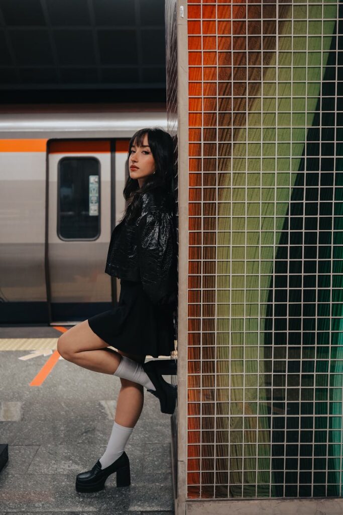 Fashionable woman in black outfit posing confidently in an urban subway station.
