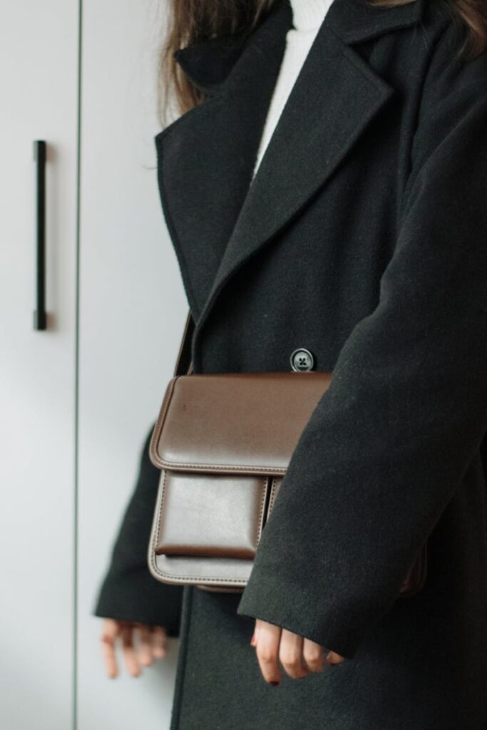 Close-up of a woman in a black coat holding a leather handbag, showcasing elegance in fashion.