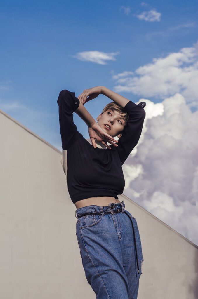 Stylish woman striking a pose in denim jeans against a vibrant cloudy sky backdrop.