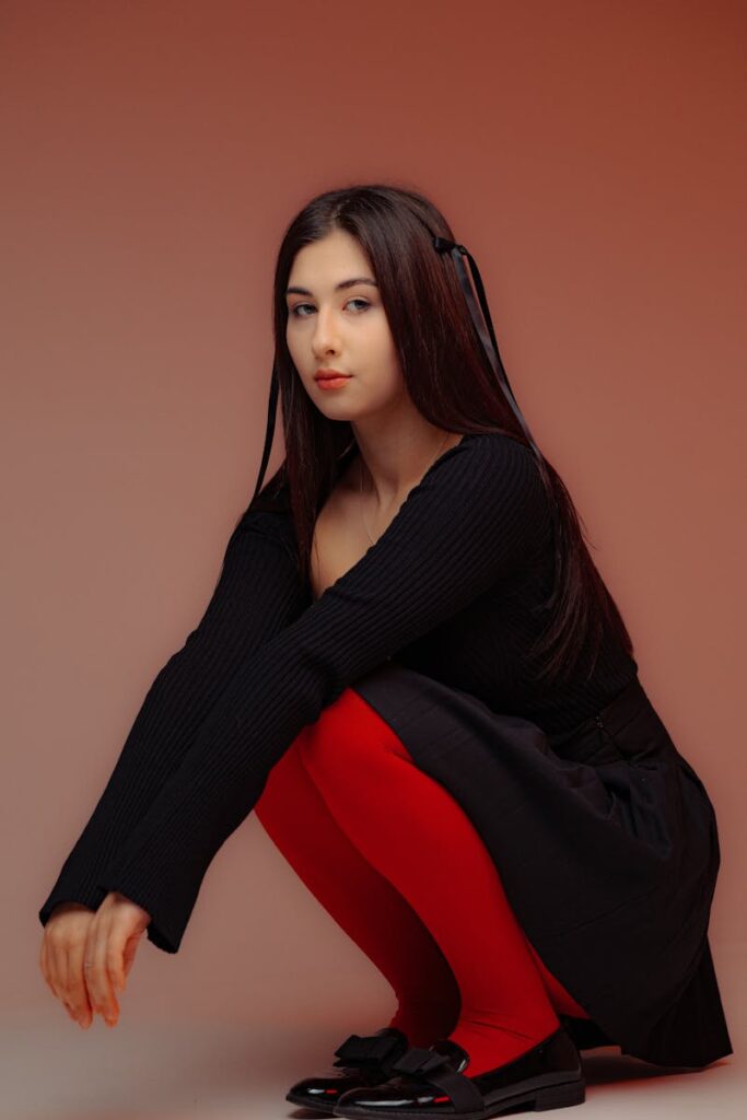 Portrait of a woman in a black dress and red tights, crouched in a studio setting.