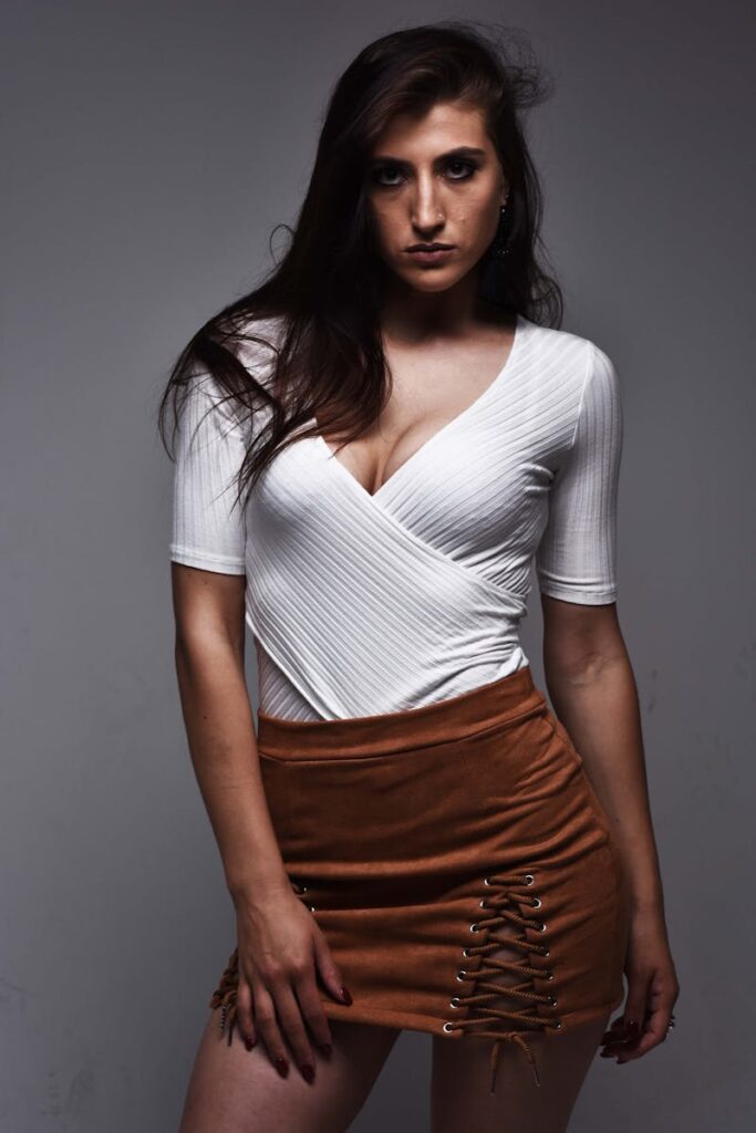 Model posing in studio with V-neck sweater and suede skirt, fashion photography.