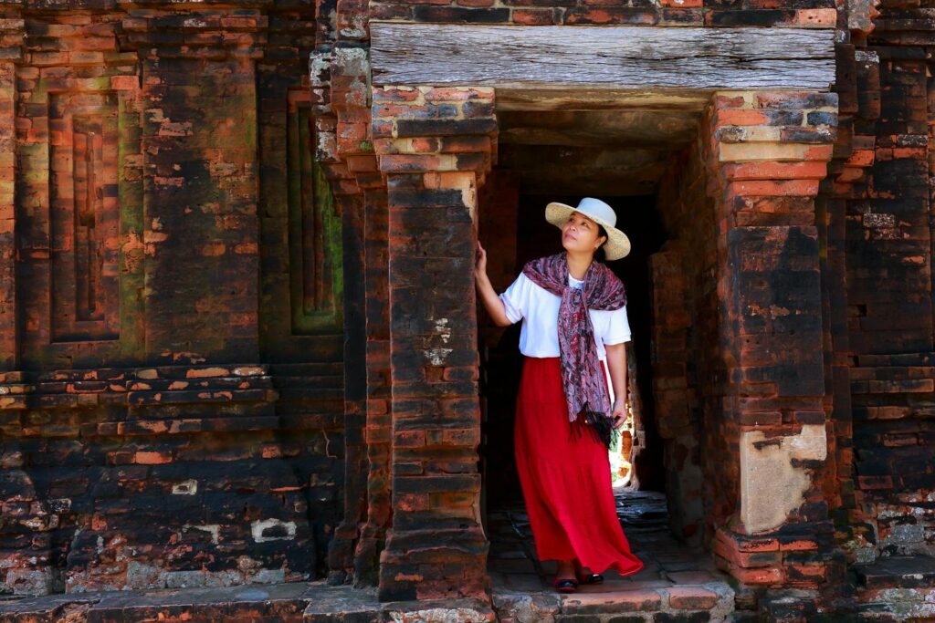 Asian woman in hat and scarf exploring an ancient stone temple entrance.