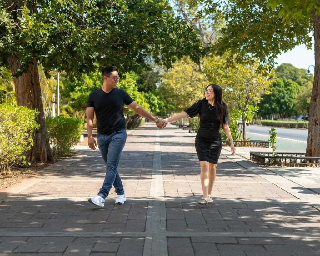 Young couple enjoying a sunny walk on a tree-lined sidewalk in Mérida, Mexico.