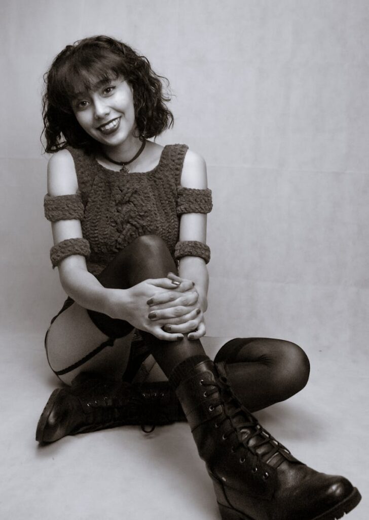 Captivating black and white portrait of smiling woman in stylish attire sitting indoors.